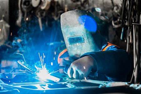 戴着铁防护面罩的焊工在一家工厂的车间从事焊接和金属工作