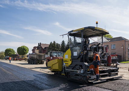 工人在道路建设和维修工程中操作沥青摊铺机。