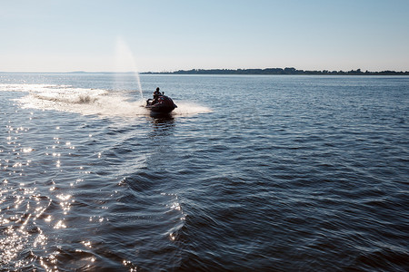 中午，强壮男子的剪影在水面上的摩托艇上跳跃。