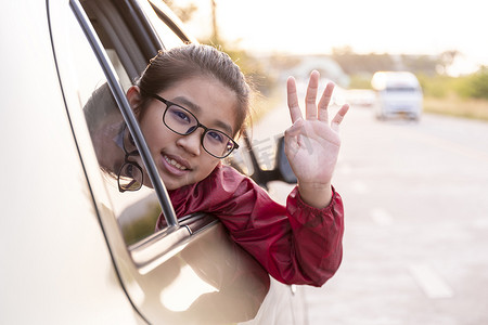 亚洲快乐的女孩挥舞着手，把头伸出车窗外。