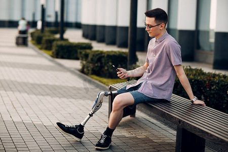 带脚假肢的残疾年轻人坐在户外拿着手机