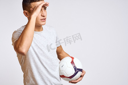 快乐的男人手里拿着球，身穿浅色背景的白色 T 恤，用双手裁剪的视角做手势