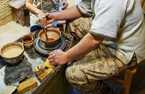 一位大师和一位学生的双手在黄色粘土的陶艺轮上制作了一个水罐。