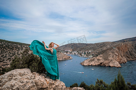 身穿翠绿色长裙的女子，身着飘逸长裙的时装模特，长着丝绸翅膀，堤岸上飞扬着织物。