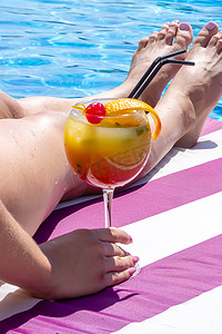 泳池边日光躺椅上的女孩喝着鲜榨橙子调制的鸡尾酒。