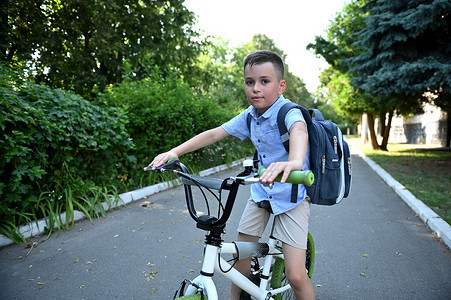 男孩骑摄影照片_骑自行车的男孩骑到学校。