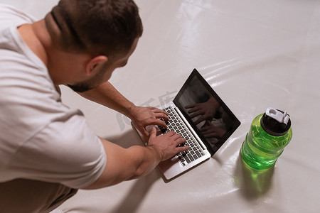 顶角英俊的男人正在寻找在线视频课程，使用笔记本电脑和准备好的瓶装水。