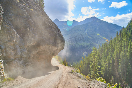 悬崖边上的公路摄影照片_悬崖边上尘土飞扬的土路危险地狭窄，山上有悬垂的岩石