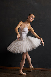 短裙脏了摄影照片_穿着白色芭蕾舞短裙的女芭蕾舞演员在黑暗背景下表演