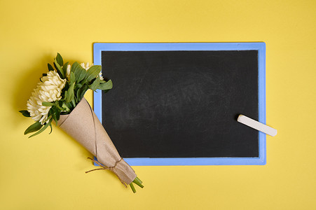 文字花卉摄影照片_平铺组合物，由精致美丽时尚的紫苑花束组成，用工艺包装纸用绳子绑在一块空白的空黑板上，黄色背景上有文字空间