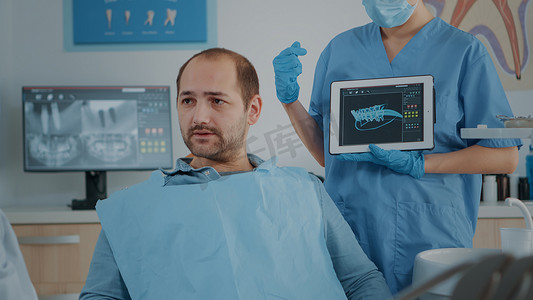 医生患者平板电脑摄影照片_牙科助理在平板电脑上向患者展示 X 射线扫描结果