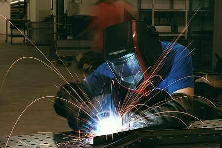 在工厂内工作的专业重工业焊工，戴着头盔并开始焊接。