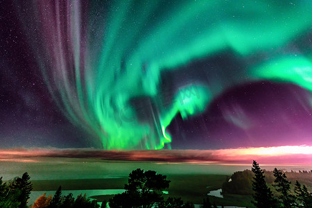 绿色大气摄影照片_北极光在部分晴朗的天空中，浓雾闪耀在瑞典山区的雾森林景观上，绿色北极光带在地平线上方弯曲，瑞典北部，斯堪的纳维亚半岛