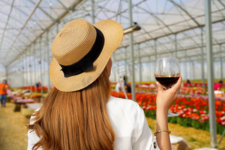 喝酒的背影摄影照片_女性在温室中举起红酒杯享受春天气氛的背影