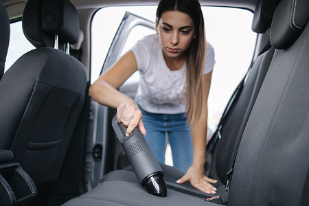 年轻漂亮的女人在她的车里使用便携式真空吸尘器。