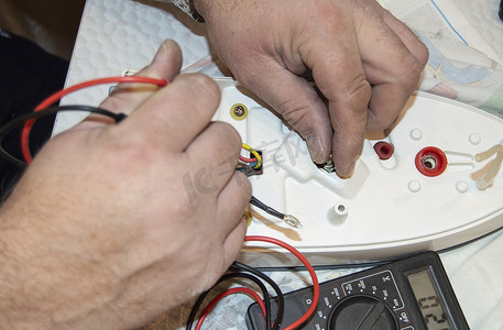 老电工手的特写，使用数字电压表修复电熨斗，选择性聚焦