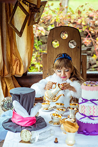 中仙境摄影照片_爱丽丝梦游仙境中一个美丽的小女孩在桌上把茶倒进杯子里的前视图