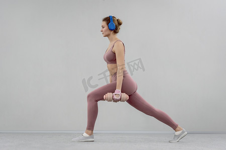 在健身房做分步伸展运动的年轻女子使用哑铃举重。