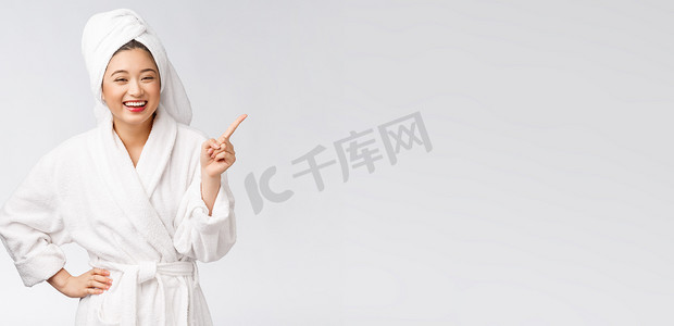 年轻女子的美丽肖像，手指指向空白的复制空间，穿着浴袍的亚洲美女。