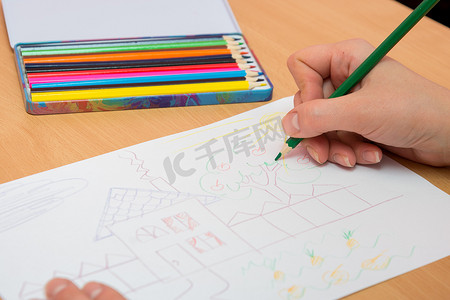 一盒铅笔摄影照片_女孩用彩色铅笔在纸上画一幅画，特写