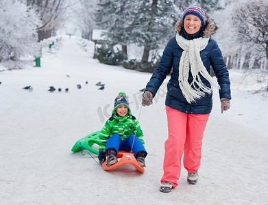 玩雪橇的孩子摄影照片_家庭在冬季公园玩雪橇
