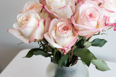 玫瑰花粥摄影照片_白桌玻璃花瓶中粉色和奶油色玫瑰的特写（裁剪和选择性聚焦）