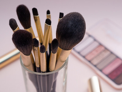 与装饰性化妆产品金色刷子和彩色眼影在柔和的粉红色背景上的组合。