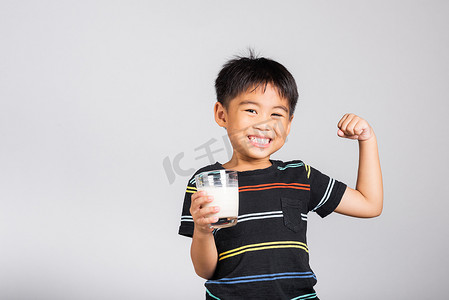5-6 岁的小可爱男孩拿着牛奶杯微笑，展示力量强大的手势