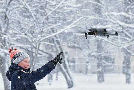十几岁的男孩穿着冬季夹克和现代数字无人机 DJI Mavic，在雪地里飞行。 