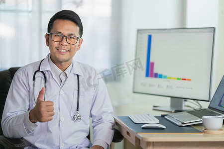 医生竖起大拇指微笑着用笔记本电脑工作男医生在办公室医院工作。