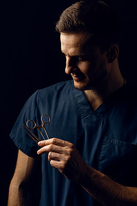 英俊的医生在深色背景上用手术剪刀。