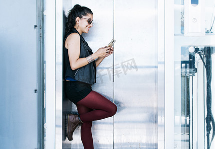 电梯里摄影照片_一个人在电梯里发短信，迷人的女孩在电梯门口用她的手机，特写城市女孩检查她的手机
