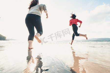 快乐的女性朋友在阳光明媚的日子里在海边跑步，朋友们快乐地放松，在傍晚日落时在海边的海滩上玩耍。