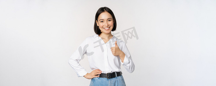 自信的亚洲女性站在白色背景上竖起大拇指表示赞同，推荐，就像 smth good 一样