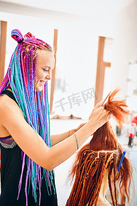 扎着彩色爆炸式辫子的美发师正在编织姜黄色长发绺。