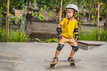 骑男孩摄影照片_戴着头盔和护膝的运动男孩在滑板公园里学习滑板。