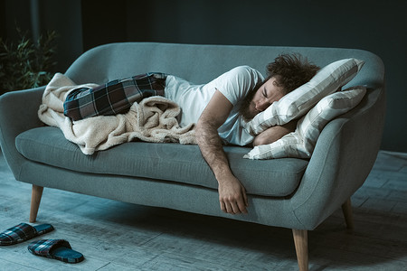 睡着的英俊男子在中午看电视时睡着了，他躺在沙发上或沙发上休息，在家享受周末或隔离日。