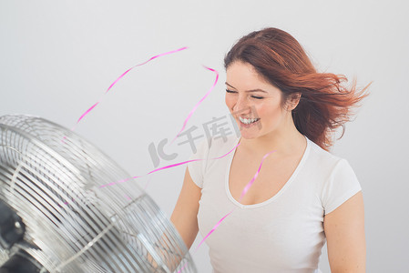 快乐的白种女人享受着白色背景下电风扇吹来的风。