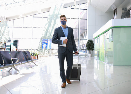 戴着防护面具的商人带着手提箱在机场大厅里。
