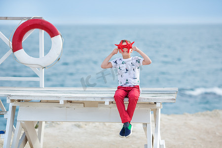 英俊的男孩青少年快乐地与他的朋友斗牛犬在海边度过时光孩子狗抱着玩两个海星靠近救生圈漂浮穿着红色裤子裤子拖鞋和 T 恤