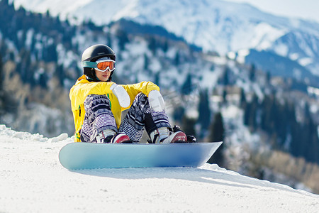 年轻女子滑雪板运动员坐在雪地里，在下降前探索斜坡