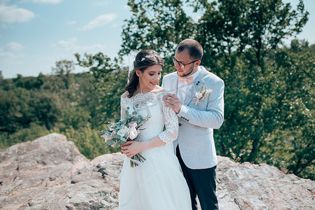 新娘和新郎在森林和岩石的大自然中以灰粉色的婚礼照片。