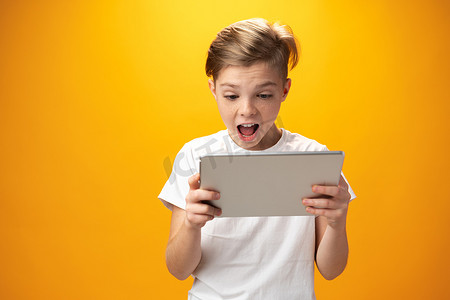 黄色背景下玩数字平板电脑的小男孩