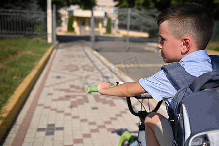 帅气的男生背着书包骑自行车去学校的画像。