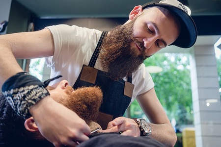 剃胡子的男人摄影照片_留着胡子的年轻人准备在有技能的美发沙龙里剃须