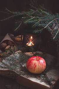 圣诞树树枝上的红黄苹果，黑灯笼或烛手附近的一本旧书，灯在燃烧