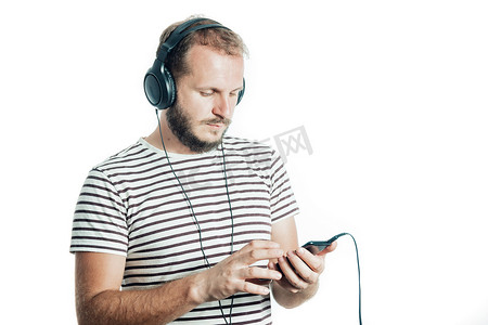 一名身穿条纹 T 恤、留着胡子的男子戴着大耳机用智能手机听音乐。 