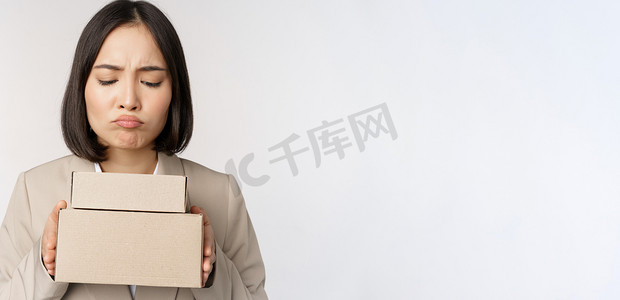 女脸手摄影照片_亚洲女售货员、女企业家拿着盒子，看上去悲伤、失望，站在白色背景上的肖像