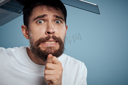 情绪化的男人，头顶上有一台打开的笔记本电脑 在蓝色背景中，穿着白色 T 恤，裁剪视图