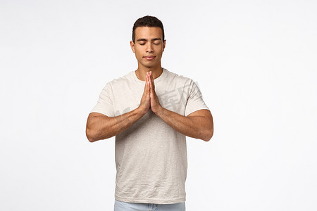 帅气健康肌肉男穿 T 恤，双手合​​十在胸前，闭上眼睛冥想，练习瑜伽，用忠实的快乐表情祈祷，吸入新鲜空气，努力寻找内心的平静